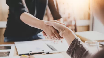 Two people shaking hands over paperwork