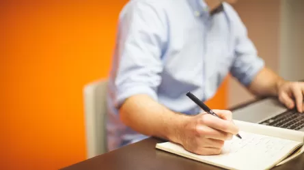 Man taking notes while working on laptop
