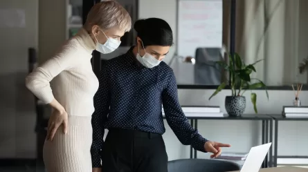 Focused two women in medical protective masks working in office.