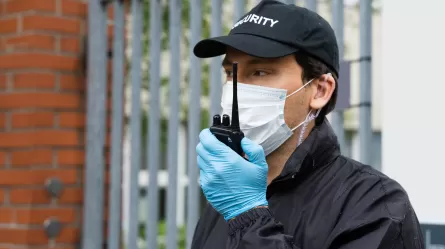 Security Guard in face mask talking on walkie talkie.