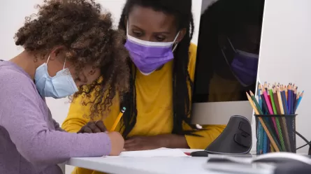 Teacher and Student sitting at desk with computer monitor and pencils and paper