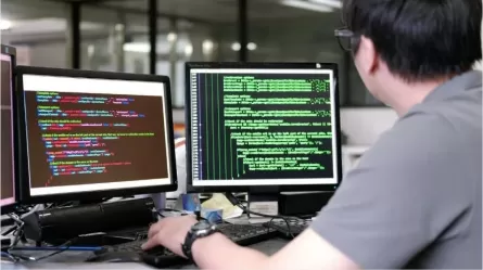 person looking at two computer monitors, keyboarding