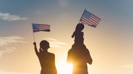man, woman and child waving U.S. flags silhouette against sunset