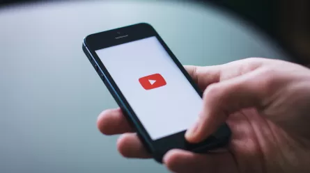 Person's hand with a cell phone. On the cell phone screen their is a red play video icon.