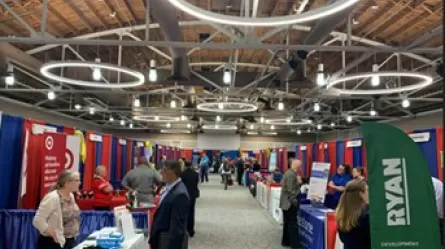 people in an exhibit hall visiting tables where people are sharing employment information