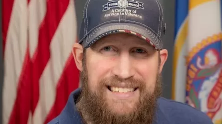 Smiling man in baseball cap in front of U.S. and Minnesota flags