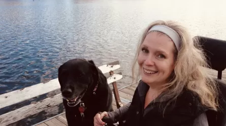 Smiling woman with dog sitting next to her and lake in the background