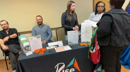 picture of staff at tables and a customer at a career fair