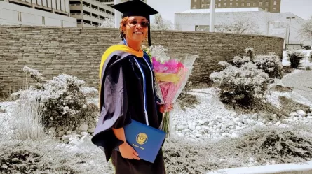 smiling woman in graduation cap and gown holding diploma and flowers