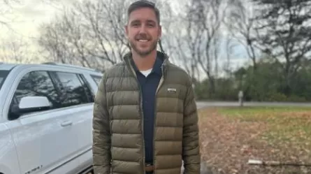smiling man in winter jacket standing next to white vehicle