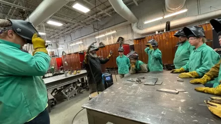 several people wearing welding helmets and protective clothing standing around a metal table in a machine shop