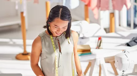 person in a tailor shop with clothing and sewing supplies in background