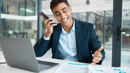 smiling person looking at a laptop and talking on a mobile phone