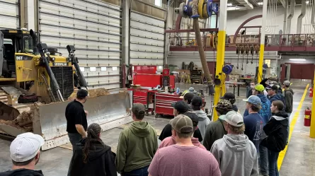 people standing in a large shop space looking at large piece of machinery