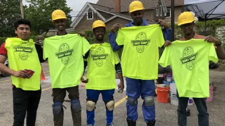 adult students wearing helmets holding up bright yellow t-shirts with the words boot camp printed on them