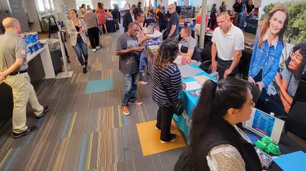 people standing and sitting in a large room lined with display tables