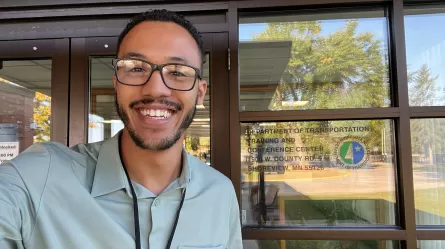 smiling man taking selfie in front of door that has MNDOT logo
