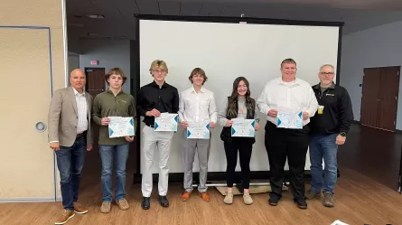 seven people standing together at the end of a large room, five of them are holding certificates