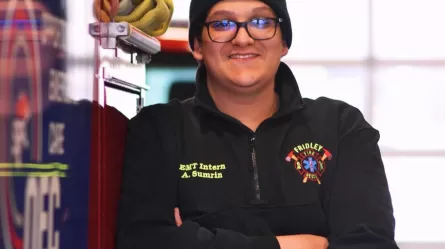 smiling person wearing glasses and a hat standing next to a fire vehicle