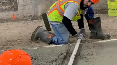 person wearing a reflective vest and hardhat measuring a section of oncrete