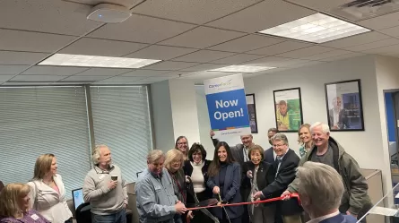 a crowd of people standing in a room with a ribbon and scissors