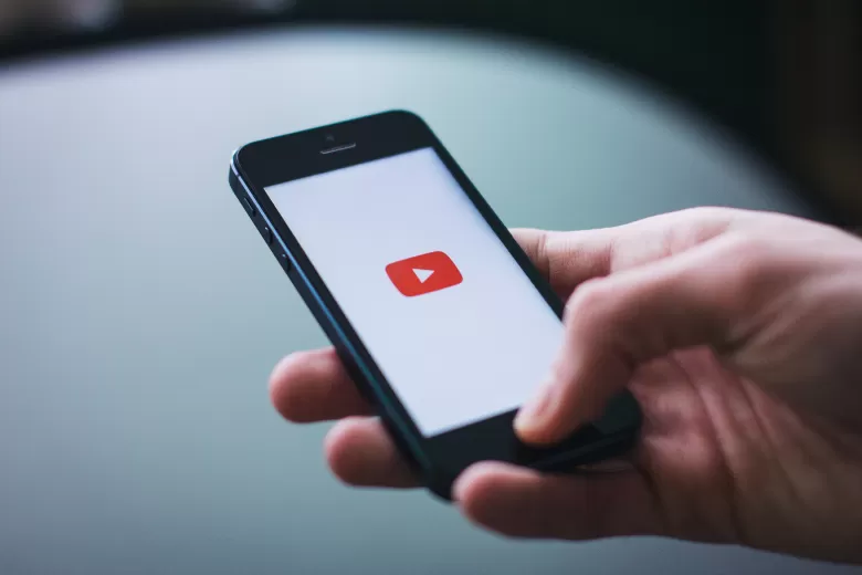 Person's hand with a cell phone. On the cell phone screen their is a red play video icon.