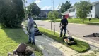 two people standing outside on a lawn, one is pushing a lawnmower, the other has a lawn trimmer in this hands