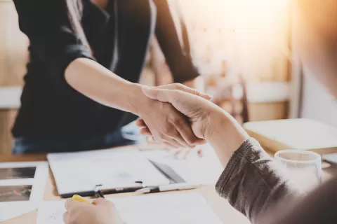 Two people shaking hands over paperwork