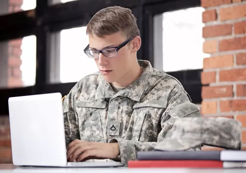 young man in military uniform on laptop