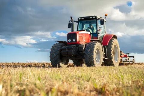 Large tractor plowing a field with worker driving on a sunny day.