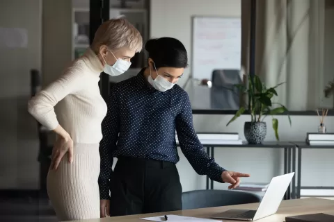 Focused two women in medical protective masks working in office.