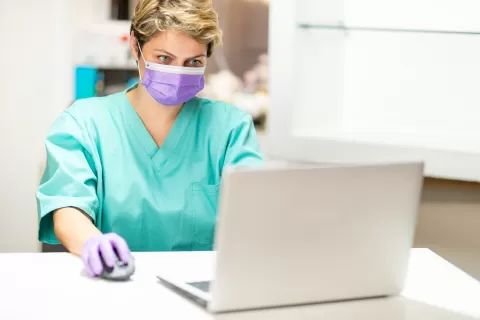 woman in medical setting on laptop, woman wearing mask