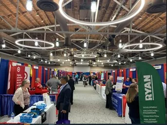 people in an exhibit hall visiting tables where people are sharing employment information