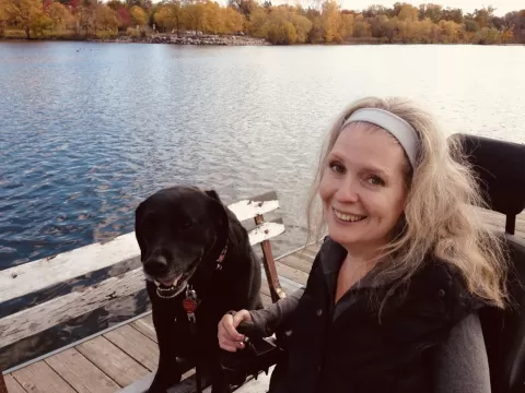 Smiling woman with dog sitting next to her and lake in the background