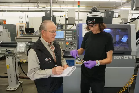 Andy Wells, a man in a vest, and Alex, a man in a stocking cap wearing gloves, at Wells Technology in Bemidji