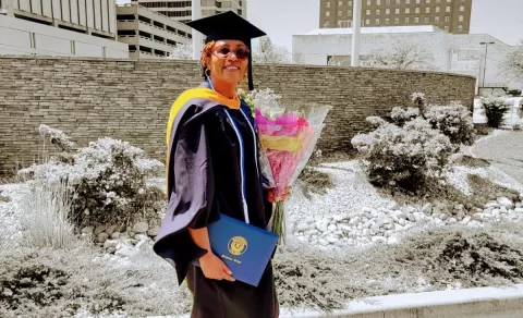 smiling woman in graduation cap and gown holding diploma and flowers