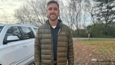 smiling man in winter jacket standing next to white vehicle