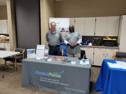 Two people standing at a table with CareerForce branded table skirt and materials