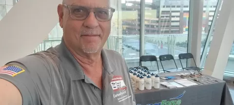 David Wold, a person taking selfie at table with CareerForce branding, water bottles and other materials
