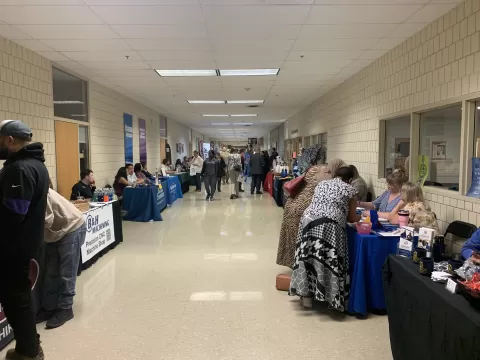 many people in a large hallway lined with display tables