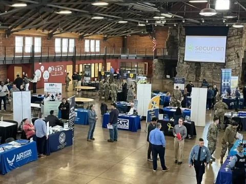 a large room with display tables and people talking to other people at the Second Annual Joint Services Career Fair