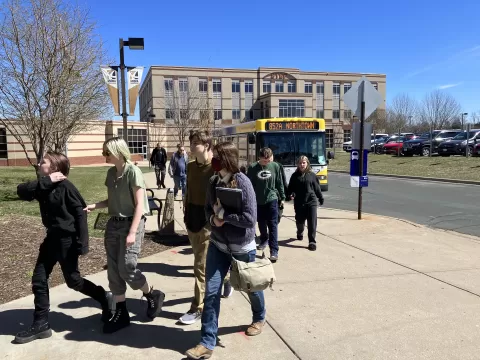 many people walking on a sidewalk with a bus in the background
