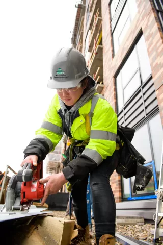person wearing hard hat and bright yellow safety jacket using a saw on a construction site