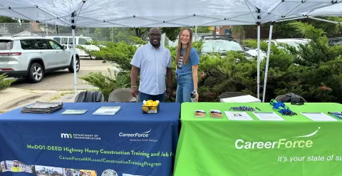 two people standing behind tables with table covers with CareerForce logo on them