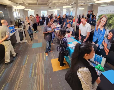 people standing and sitting in a large room lined with display tables