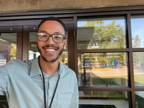 smiling man taking selfie in front of door that has MNDOT logo