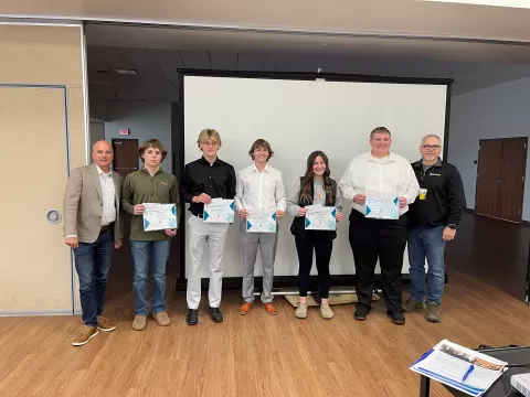 seven people standing together at the end of a large room, five of them are holding certificates