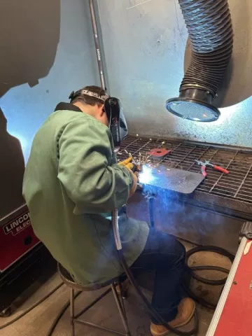 person wearing protective gear and welding something on a work bench