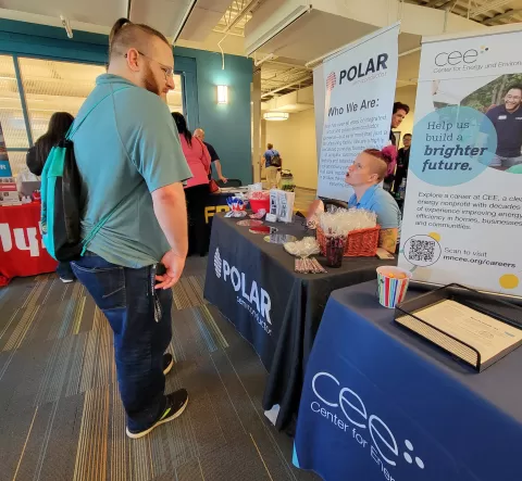 Standing person talking to sitting person at an employer booth at the 9-26-24 veterans and community job and resource fair. There is a banner that reads Polar at the booth.