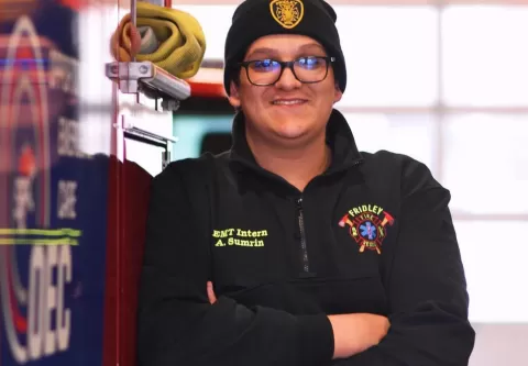 smiling person wearing glasses and a hat standing next to a fire vehicle